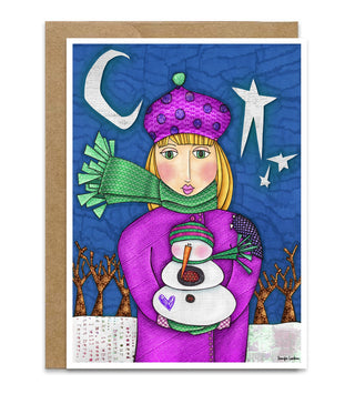 A winter-themed greeting card featuring a stylized illustration of a girl in a purple coat and hat with a green scarf, holding a snowman, set against a blue night sky with stars and a crescent moon. The card is shown with a brown kraft envelope behind it on a white background. Artwork by Jennifer Lambein.