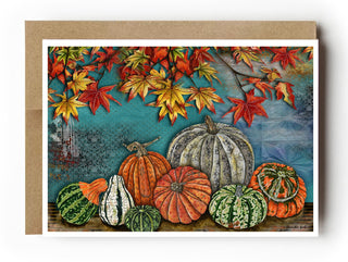 Aa autumn greetingcard featuring an autumn harvest scene with pumpkins and gourds beneath red and yellow fall leaves, shown against a blue sky background with a kraft envelope behind it.
