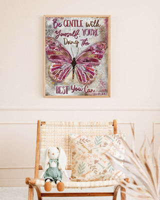 Framed butterfly poster with motivational quote above a wooden chair with a plush toy and pillow.