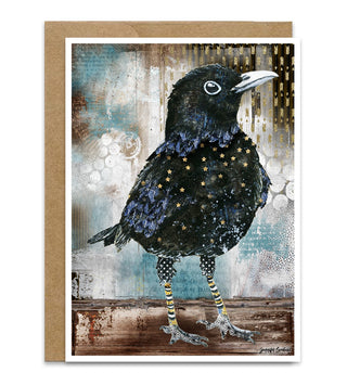 A greeting card featuring a watercolor black bird with blue iridescence,  gold stars, and striped legs, shown with a brown kraft envelope behind it on a white background.  Artwork by Jennifer Lambein. 