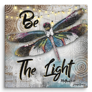 A canvas print with a whimsical dragonfly on it that says, "Be the light. Mathew 5:15." Artwork by Jennifer Lambein. 