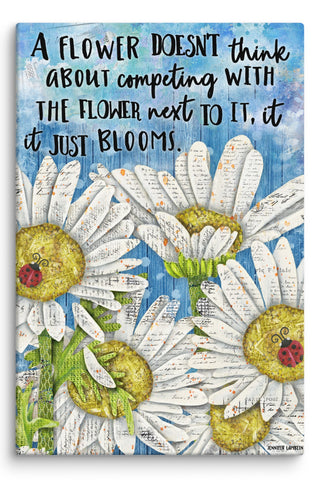 A canvas print with daisies and ladybugs on a blue sky background that says, "A flowers doesn't think about competing with the flowers next to it, it just blooms. " Artwork by Jennifer Lambein. 