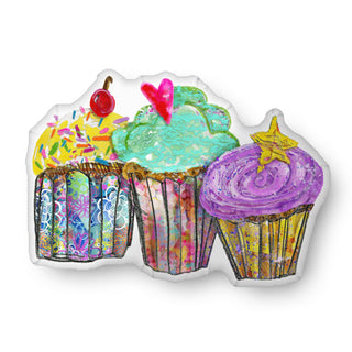 A throw pillow in the shape of three whimsical cupcakes. They have a star, cherry, and heart on top. Artwork by Jennifer Lambein. 