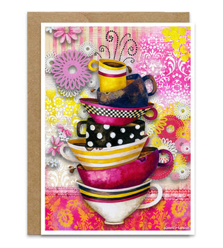 A greeting card featuring a colorful stack of coffee and teacups and floral patterns, shown with a brown kraft envelope behind it. Artwork by Jennifer Lambein. 