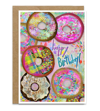 A birthday card with a kraft envelope, featuring a colorful illustration of donuts with sprinkles and the words 'Happy Birthday!' in blue and purple script. Artwork by Jennifer Lambein. 