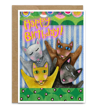 A colorful birthday card featuring five playful illustrated cats under the text 'Happy Birthday!' in pink, shown with a brown kraft envelope on a whimsical blue and white striped background. Artwork by Jennifer Lambein. 