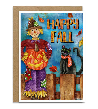 An autumn-themed greetingcard featuring a smiling scarecrow holding a carved pumpkin, a black cat wearing a red-and-white scarf, and the words “HAPPY FALL” in large orange letters. The print is shown with a kraft envelope behind it on a white background. Artwork by Jennifer Lambein. 