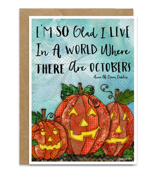 A greeting card with a kraft envelope, featuring a watercolor-style illustration of three carved pumpkins and the quote, 'I'M SO Glad I LIVE In A WORLD Where THERE Are Octobers' from Anne Of Green Gables. Artwork by Jennifer Lambein. 