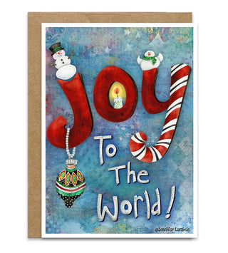 A Christmas greeting card with a kraft envelope, featuring the word 'joy' in large red letters decorated with a holiday snowman, bird, and ornament, and the phrase 'To The World!' in white script on a blue watercolor-style background. Artwork by Jennifer Lambein. 