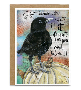 A greeting card with a kraft envelope, featuring an illustration of a black raven perched on a cream-colored pumpkin with a quote that says, "Just because you can't see it, doesn't mean you can't believe it." Artwork by Jennifer Lambein. 