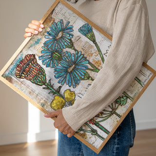 Person holding a framed artwork with floral designs