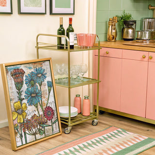 Kitchen with a gold bar cart, floral artwork, and pink cabinets.