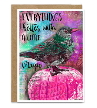 A greeting card with a kraft envelope, featuring a colorful artistic design of a raven bird perched on a pink pumpkin with the text 'EVERYTHING'S better with A LITTLE Magic'. Artwork by Jennifer Lambein. 