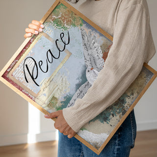 Person holding a framed piece of art with the word 'Peace' on it.