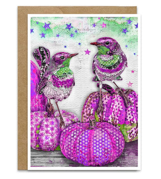A greeting card featuring a whimsical illustration of two purple and green birds perched on purple patterned pumpkins, set against a textured white background with a brown kraft envelope behind it. Artwork by Jennifer Lambein. 