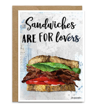 A greeting card with a kraft paper envelope, featuring the text 'Sandwiches ARE FOR lovers' above an illustration of a loaded sandwich with bacon, lettuce, tomato, and cheese on a textured light blue and white background. Artwork by Jennifer Lambein. 