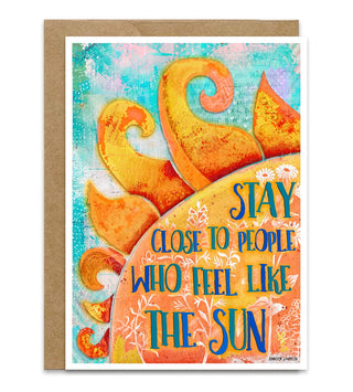 A greeting card with a kraft paper envelope, featuring a colorful abstract sun design with the text 'STAY CLOSE TO PEOPLE WHO FEEL LIKE THE SUN' in blue and orange lettering. Artwork  by Jennifer Lambein. 