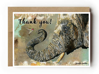 A greeting card with a kraft envelope behind it, featuring a watercolor elephant and hummingbird with the words 'Thank you!' on a white background. Artwork by Jennifer Lambein. 