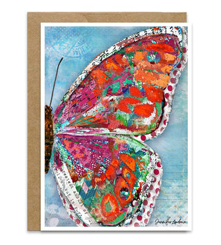 A greeting card featuring a colorful butterfly wing with red, orange, green, and pink patterned wings on a light blue textured background, shown with a kraft envelope behind it. Artwork by Jennifer Lambein. 